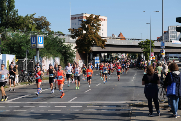 Eine Gruppe von Menschen, die einen Marathon auf einer von Bäumen gesäumten Straße unter einem klaren blauen Himmel laufen.