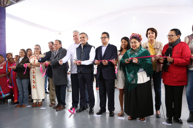 Menschen schneiden ein Band bei einer Bandschneidezeremonie, stehen vor einer Menge mit einer Säule links, Papieren auf dem Boden und einem weißen Tuch im Hintergrund.