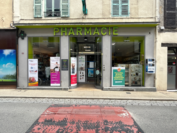 Eine Apotheke an einer Straßenecke mit Glaswänden und Türen, Plakate an den Wänden und eine Straße davor.
