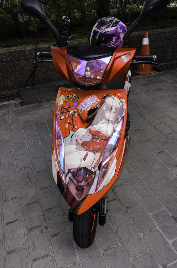 Ein oranger Roller mit einem Helm darauf auf einer Straße geparkt, mit einem Verkehrskegel, einer Wand und Bäumen im Hintergrund.