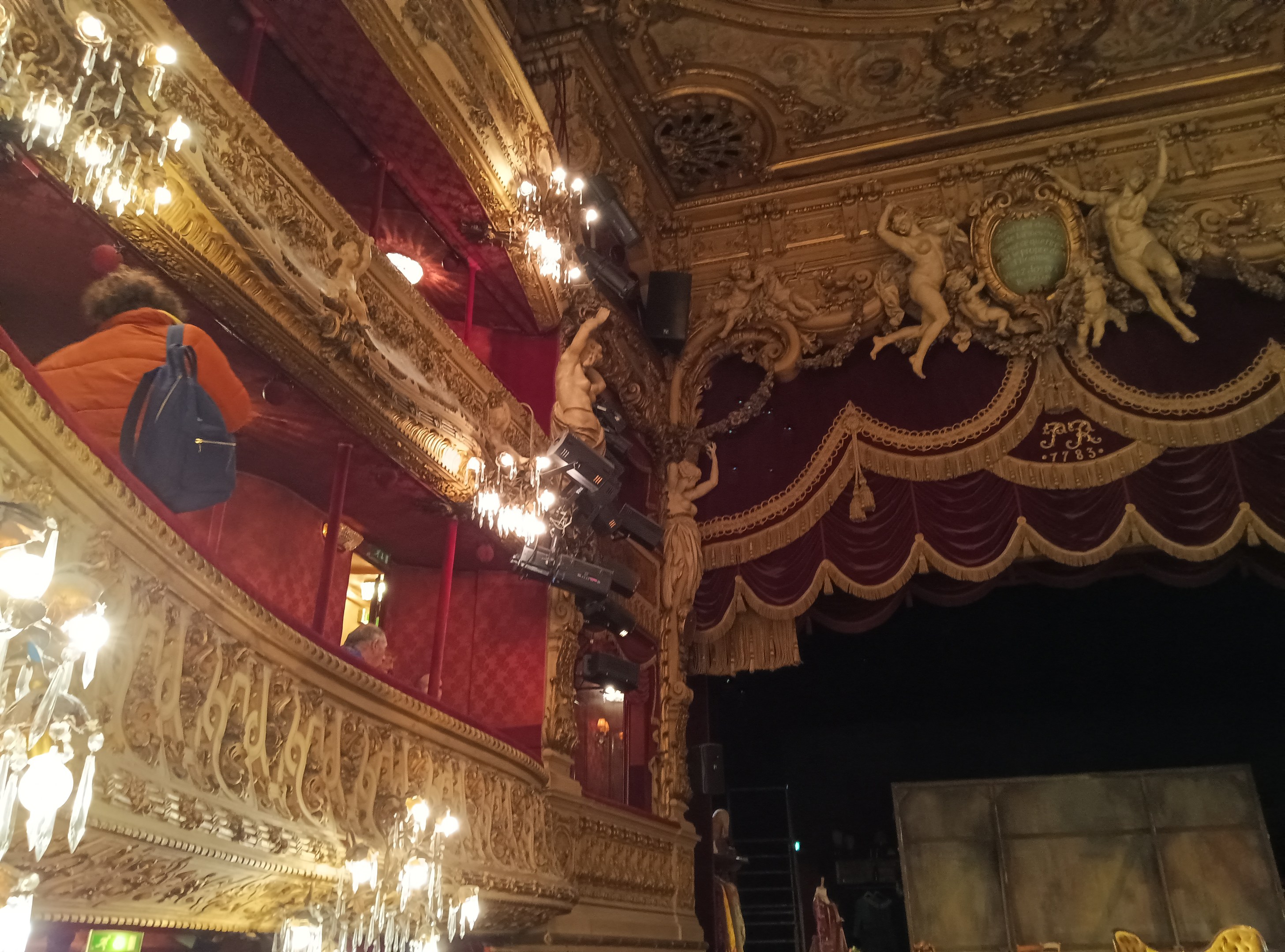 Gemälde namens "Tanz am Moulin Rouge" von Edgar Degas zeigt tanzende Frauen in weißen Kleidern und bunten Kostümen auf einer Bühne mit einem lebhaften blauen Hintergrund und warmem gelbem Licht.