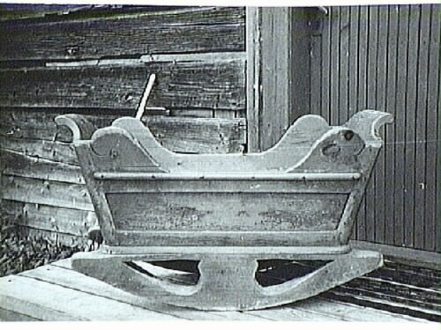 Schwarzes und weißes Foto eines alten Holzschaukelstuhls auf einer Holzveranda mit einer Holzwand im Hintergrund.