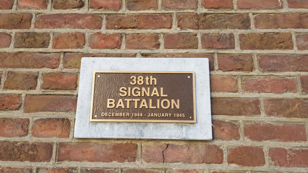 Eine Ziegelwand mit einer rechteckigen Plakette, auf der in fetter, weißer Schrift "38. Signalbataillon" steht.