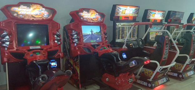 Eine Reihe buntfarbiger Arcade-Rennwagenautomaten auf einem gefliesten Boden mit einer Wand im Hintergrund.