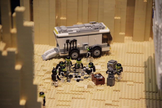 Lego-Modell einer Star Wars-Szene mit einem Landfahrzeug im Vordergrund und einer Wand im Hintergrund, umgeben von verstreuten Lego-Spielzeugen.