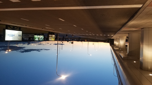 Ein Indoor-Schwimmbad umgeben von Säulen auf der rechten Seite, mit einer Decke, die Lichter und Bildschirme im Hintergrund zeigt.
