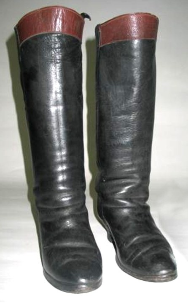 Schwarze Stiefel mit roter Sohle, glänzendes Lederobermaterial, tiefe rote Schnürsenkel, niedriger Absatz und rundes Zehenende auf einer weißen Oberfläche.