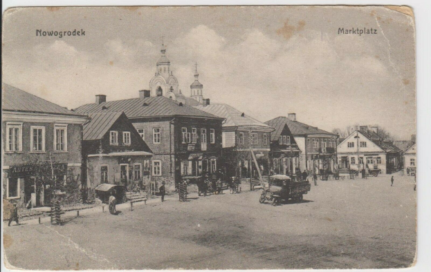 Schwarz-weiß-Foto einer Stadtstraße in Nowogrodeek, Deutschland, mit Gebäuden, Menschen, Karren, Pfählen, Bäumen und Himmel, mit der Beschriftung "Marktplatz in Nowogrodeek, Deutschland" oben und unten.