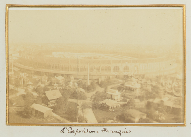 Altes Schwarz-Weiß-Foto eines Stadions inmitten einer städtischen Umgebung, umgeben von Gebäuden, Bäumen und Strommasten, mit unten sichtbarem Text.