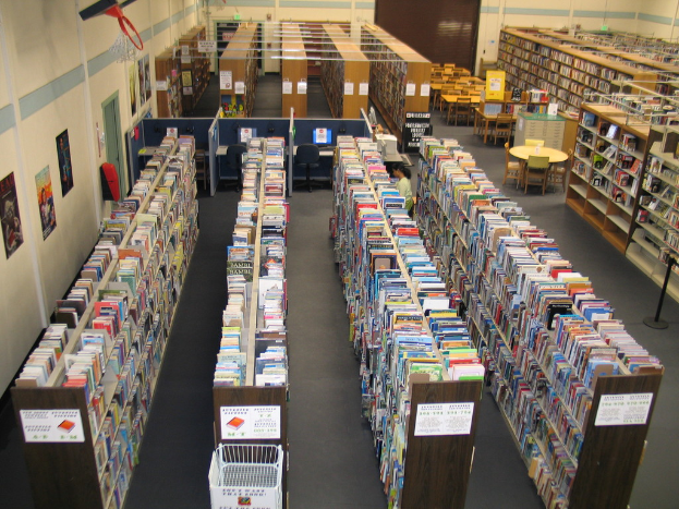 Ein Bibliothek-Innenraum mit Bücherregalen voller Bücher und Tischen und Stühlen vor einer Wand.