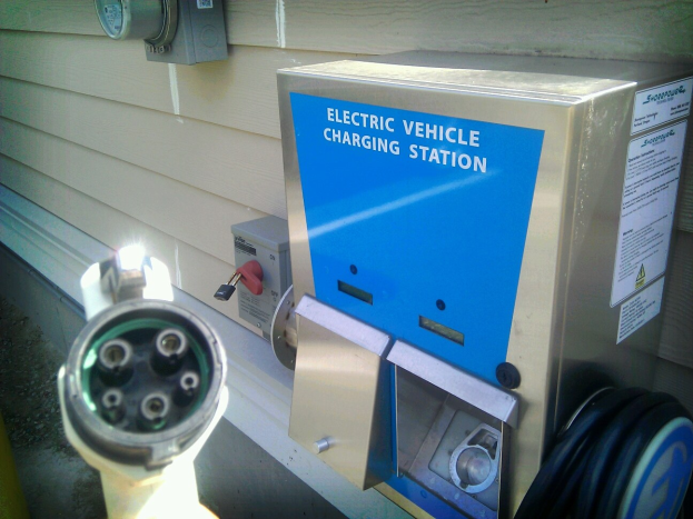 Elektrofahrzeug-Ladestation an der Seite eines Gebäudes mit angeschlossenem Ladekabel und zusätzlichen wandmontierten Objekten im Hintergrund.