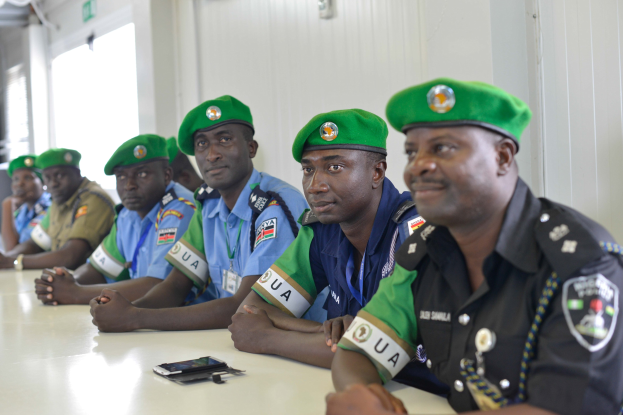 Eine Gruppe von Polizeibeamten an einem Tisch während einer Schulung, mit Mobiltelefonen und anderen Gegenständen auf dem Tisch, in einem Raum mit Fenstern und Deckenleuchten.