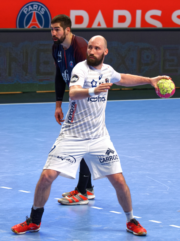 Zwei MÃnner beim Handballspielen auf einem Platz, einer hÃlt einen Ball, mit einer Tafel im Hintergrund, auf der "Paris Saint-Germain vs Paris Saint Germain" steht.