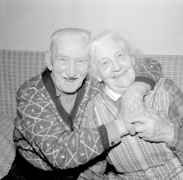 Schwarz-weißes Foto eines älteren Paares auf einem Sofa sitzend, das sich umarmt und lächelt.