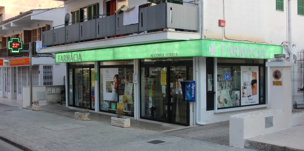 Eine Straßenecke mit einer Apotheke und umliegenden Gebäuden, Fahrzeugen und einem klaren blauen Himmel.
