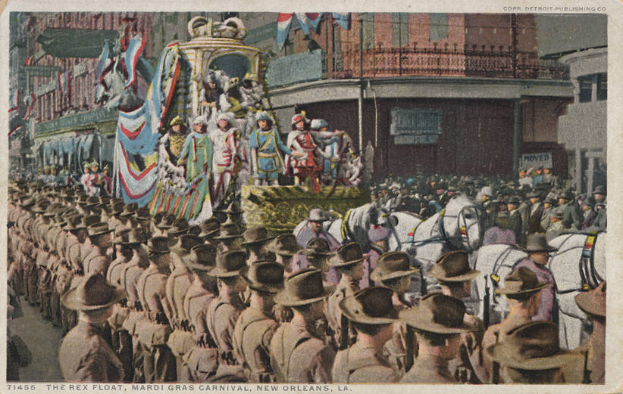 Eine alte Postkarte, die einen Mardi Gras-Umzug in New Orleans zeigt, mit einem mit Fahnen und anderen Dekorationen geschmückten Festwagen, Menschen zu Pferd und Zuschauern am Straßenrand, sowie im Hintergrund Gebäude mit Fenstern und Geländern.