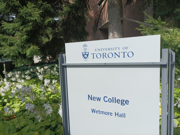Das neue College der Universität Toronto am Wetmore Hall mit einem Schild davor, umgeben von grünem Gras, bunten Blumen, hohen Bäumen und einem hellblauen Himmel.