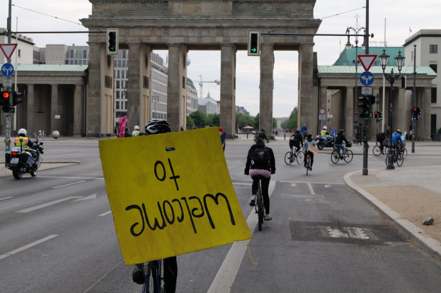 Eine Gruppe von Menschen, die auf Fahrrädern die Straße vor dem Brandenburger Tor in Berlin, Deutschland, entlangfahren, mit einer Person, die ein gelbes Schild hölt.