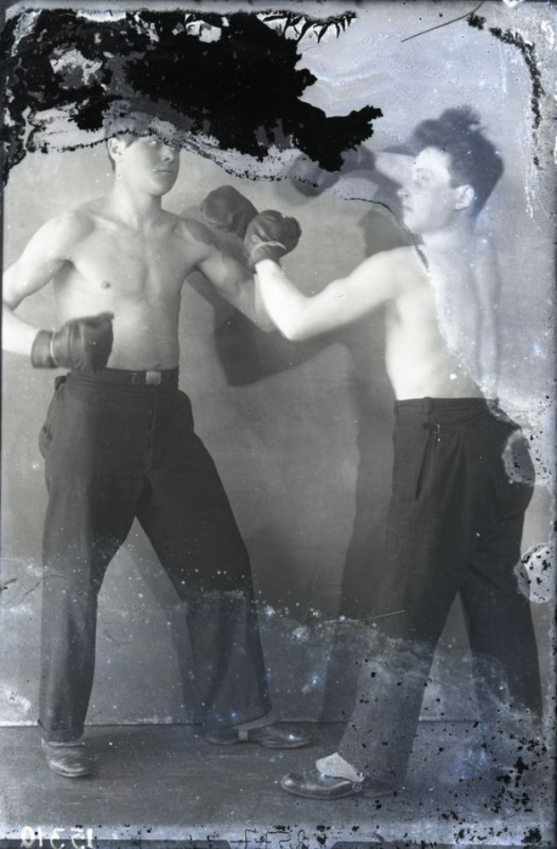 Zwei Männer in schwarzen und weißen Boxhandschuhen stehen auf dem Boden bereit, um zu boxen.
