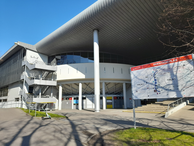 Ein großes Gebäude mit vielen Fenstern, Säulen und Treppen, das als Eingang zum Olympiastadion in London dient, mit einem Karren, Gras, einer Straße, Bäumen und einem Himmel im Hintergrund.