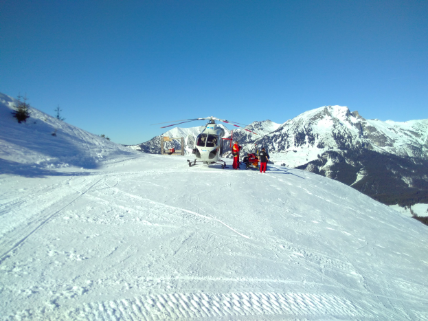 Ein Hubschrauber auf einem schneebedeckten Berg mit einigen Menschen in der Nähe, unter einem klaren Himmel.
