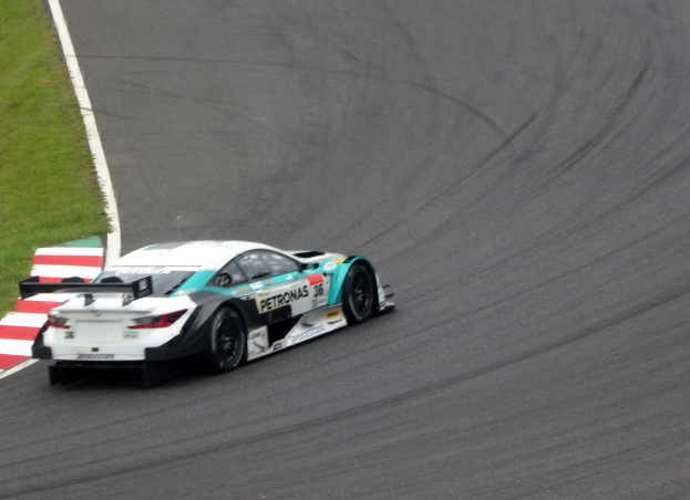 Ein silberner Mercedes-AMG GT3-Rennwagen mit Sponsorentext auf der Karosserie auf einer Rennstrecke fahrend, mit Gras links sichtbar.