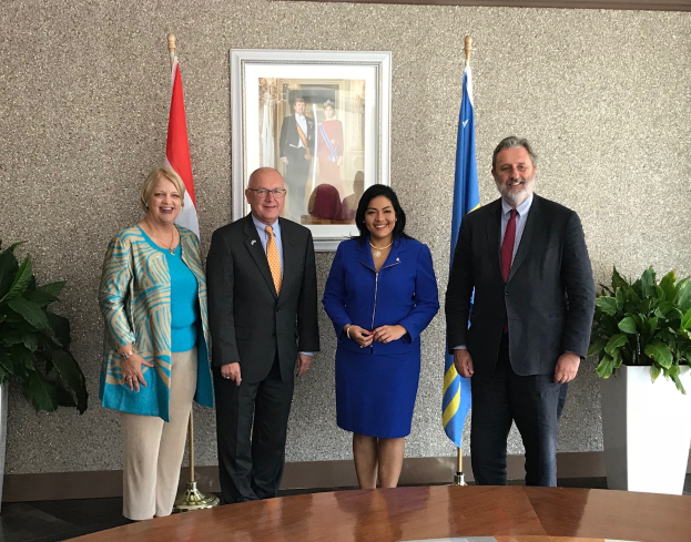 Eine Gruppe strahlender Menschen um einen Tisch mit Papieren herumstehend, umgeben von Fahnen, Topfpflanzen und einem Foto auf dem Wand, feiern die Unterzeichnung eines Memorandums zwischen den Vereinigten Staaten und Kanada.