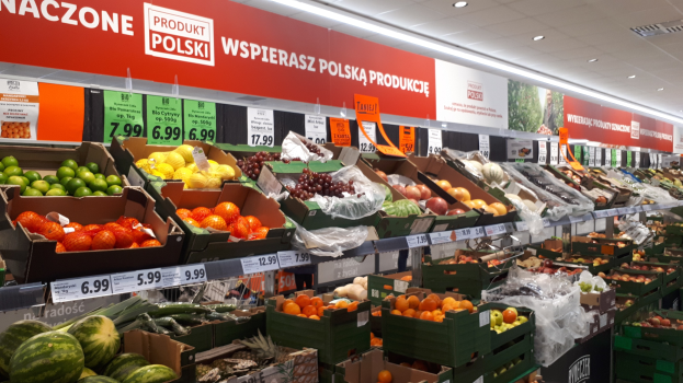 Ein Geschäftsraum mit verschiedenen Früchten und Gemüsen in Kartons mit Preisschildern, Informationsschilder an den Wänden und Deckenbeleuchtung.