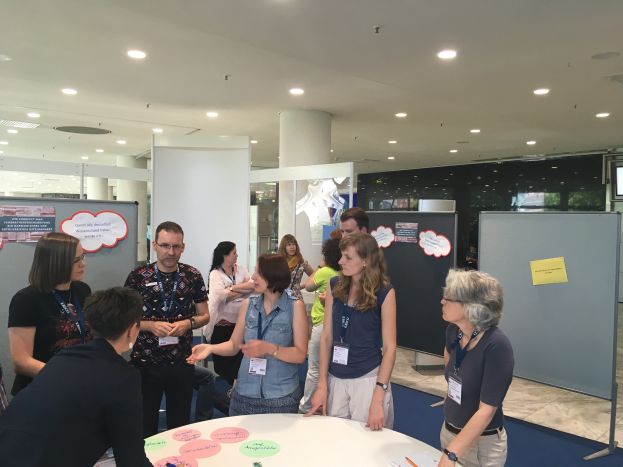 Eine Gruppe von Menschen mit Namensschildern steht um einen Tisch mit Papieren und Gegenständen in einem Raum mit Tafeln, einer Säule und Deckenleuchten, was auf eine Konferenz in Madrid, Spanien im Jahr 2019 hindeutet.
