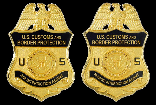 Zwei goldfarbene Abzeichen mit dem Text "U.S. Customs and Border Protection" auf einem weißen Hintergrund.