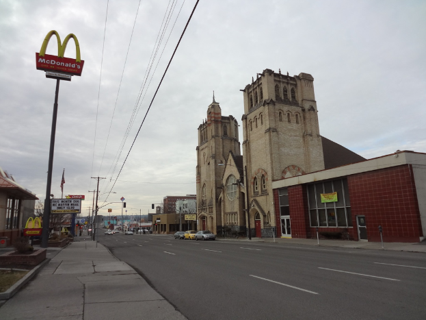 Eine Straßenansicht mit Gebäuden auf der rechten Seite, Masten und Autos in der Mitte und einem McDonald’s-Mast auf der linken Seite.