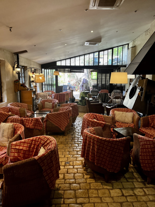 Ein geräumiger Eingangsbereich mit Stühlen, Tischen, Sofas mit Kissen, Wandlampen, einer Deckenklimaanlage und Glasfenstern an der Rückseite.