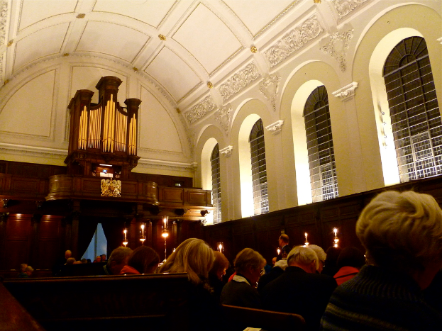 Das Innere einer Kirche mit sitzenden Menschen und Kerzen davor, mit weißen Wänden und Decke.