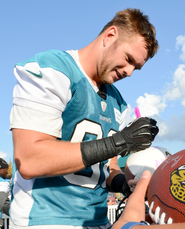 Jacksonville Jaguars-Quarterback Blake Bortles in einem blauen und weißen Trikot signiert Autogramme für Fans, umgeben von einer Menge mit einigen, die Mützen tragen, unter einem Himmel voller weißer, flauschiger Wolken.